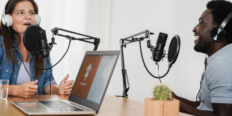 Two people sitting opposite each other wearing headphones and talking into microphones recording a podcast